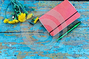 Top view image of open notebook on the old blue painted wooden table with yellow flowers. Blank notebook with flower and green pen