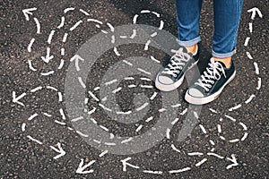 top view image of person in jeans and retro shoes standing over asphalt road with painted arrows showing different directions. photo