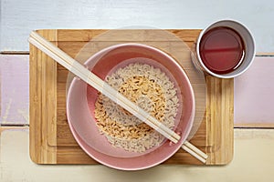 Top view image of pink bowl with Chinese curly noodles, chopsticks