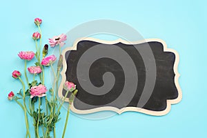 Top view image of pink flowers composition and empty blackboard over blue pastel background