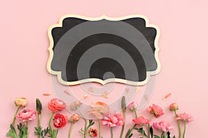 Top view image of pink flowers composition and empty blackboard over pastel background