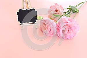 Top view image of pink flowers composition and empty blackboard over pastel background