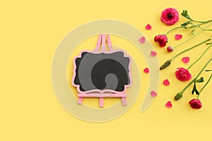 Top view image of pink flowers composition and empty blackboard over yellow pastel background