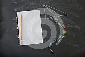 Top view image of plane sketch next to empty notebook paper over classroom blackboard background.