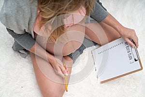 Top view image of pregnant woman holding birth plan checklist and pencil while sitting on her bed at home