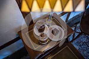 Top view image of a slice of brownie cake with glass of coffee on a vintage wooden table