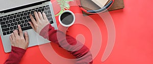 Top view image of smart man`s hands typing on computer laptop keyboard that putting on red working desk.