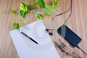 Top view image of smartphone with blank screen headphones, earphone and white paper with pen on wood table background, concept