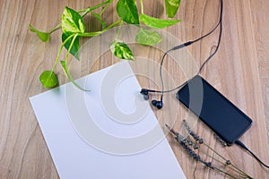 Top view image of smartphone with blank screen headphones, earphone and white paper with pen on wood table background, concept