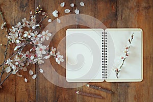 Top view image of spring white cherry blossoms tree next open blank notebook on wooden table. vintage filtered and toned image