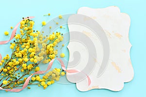 Top view image of spring yellow mimosa flowers composition over pastel blue background