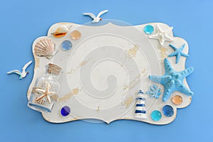 Top view image of starfish, shells, sea glass and empty white board over blue background