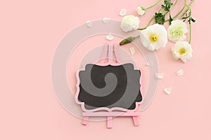 Top view image of white flowers composition and empty blackboard over pink pastel background