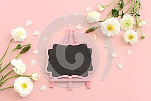 Top view image of white flowers composition and empty blackboard over pink pastel background