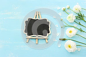 Top view image of white flowers composition and empty blackboard over wooden blue pastel background