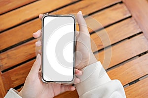 Top view image of a woman's hand holding a white-screen smartphone mockup over a wooden table