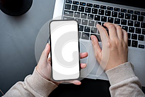 A top view image of a woman typing on laptop keyboard and holding a white-screen smartphone mockup