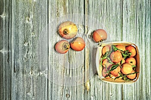 Top view image of wooden basket with ripe fruit, mandarinas with green leaves, persimmons and pomegranate
