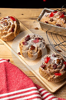 Top view of individual plum cakes, decorated with sugar, raisins and cherries, on wooden table with rustic red cloth,