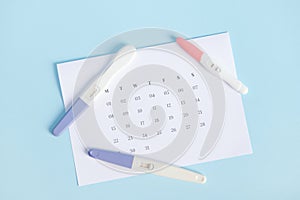 Inkjet pregnancy tests on white calendar with marked dates in last menstruation. Calculation of ovulation day. Top view photo