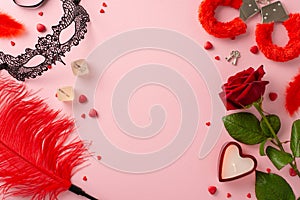 Top view intimate essentials lace mask, dice game, furry handcuffs, feather tickler, red rose, candle on pink backdrop