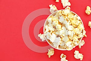 Top view isolated salted popcorn mix with cheese popcorn spilled from white bowl on red table background, movie cinema time