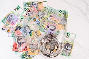 Top view of a jar with coins and Australian dollar banknotes on the white background