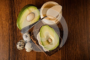 Top view on jar with tahini, rye bread, sliced avocado, and quail eggs