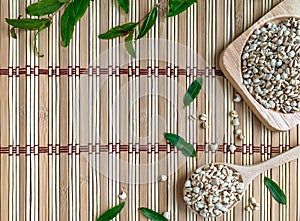 Top view of Job`s Tears or Millet on a tray and a wooden spoon. The background is a wooden mat decorated with pomegranate leaves