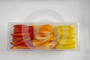 Top view of Julienne sliced colorful bell peppers in a clear plastic tub on a white tray