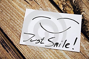Top view of Just Smile sticky note on the wooden desk with smile face.