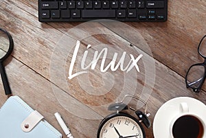 Top view of Keyboard,magnifying glass,notebook,pen,clock,a cup of coffee and sunglasses on wooden background written with Linux