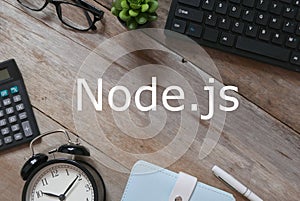 Top view of keyboard,plant,sunglasses,pen,notebook,clock and calculator on wooden background written with Node.js photo