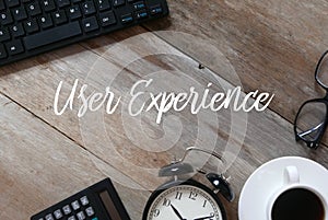 Top view of keyboard, sunglasses, a cup of coffee, clock, and calculator on wooden background written with User Experience