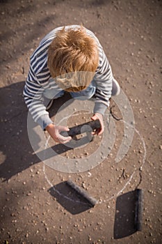 Top view on kid boy playing skittles in the street. Russian game skittles. Wooden skittles. Outdoor activites with children. Child