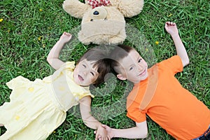 Top view of kids lying on the grass at park having fun. Little girl and boy relax with smiling. Teddy bear toy