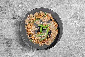 Top view Korean kimchi fried rice topping white sesame and seaweed in a black bowl on the grey concrete table, close-up shot