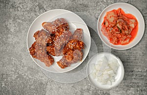 Top view Korean spicy deep-fried chicken topped white sesame with kimchi and pickled radish side dishes on the gray concrete table