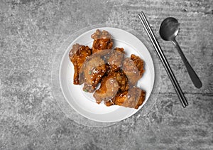 Top view Korean spicy deep-fried chicken topped white sesame with a spoon and chopsticks on the gray concrete table, popular stree