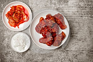 Top view Korean spicy fried chicken with side dishes on gray concrete table.