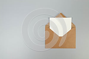 Top view of kraft brown envelope, white card on grey background.