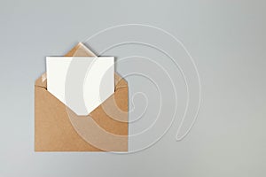 Top view of kraft brown envelope, white card on grey background.