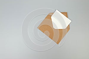 Top view of kraft brown envelope, white card on grey background.