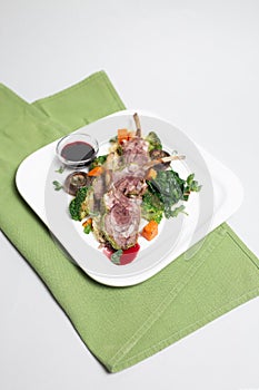 top view of a lamb rack with baked vegetables and microgreens on a white plate.