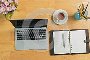 Top view of Laptop with blank screen, pencils, notebook, vase and tea on table in home office. Workspace with laptop and office