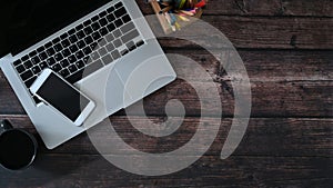 Top view of laptop computer, smart phone and notebook on wooden table.