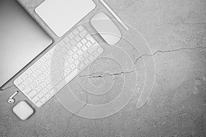 Top view of laptop computer, white keyboard, mouse, touchpad, earphones case, pen on concrete background.