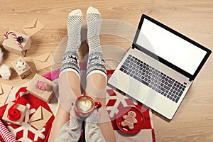 Top view of laptop in girl`s hands sitting on a wooden floor with cup of coffee, christmas decoration, gifts and wrapping paper