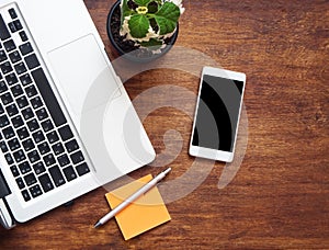 Top view of laptop keyboard, orange sticker with pen and cellphone on the wooden table