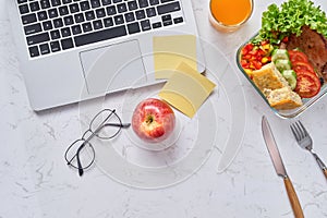 Top view of laptop, orange juice in glass and fresh salad in lun